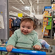 Nevaeh is registered to the contest to win money with this photo: baby, bodypart, clothing, face, finger, grocerystore, hand, happy, head, indoors, knitwear, market, person, photography, portrait, shelf, shop, shopping, shoppingcart, sweater