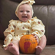 Aliana is registered to the contest to win money with this photo: baby, infant, pumpkin, smiling, cute, headband, autumn, fall, holiday, orange, clothing, sitting, couch, foot, hand, face, happy, child, portrait, home