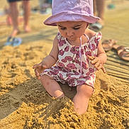Cel a rejoint le concours — aidez-le/la à gagner de superbes lots ! beach, blurred_background, child, exploration, footwear, fun, hands, legs, nature, outdoor, people, pink, play, romper, sand, summer, sunhat, sunlight, toddler, vacation