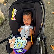 Lyam a rejoint le concours — aidez-le/la à gagner de superbes lots ! baby, car_seat, plush_toy, outdoor, pavement, autumn_leaves, baby_clothing, child, seat_belt, toy, person, feet, black_car_seat, infant, sitting, sun_pattern, colorful_toy, handle, safety, young_child