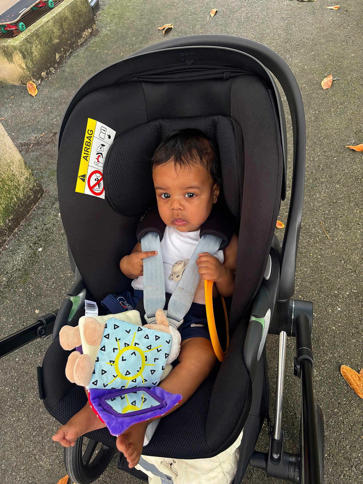 Lyam a rejoint le concours — aidez-le/la à gagner de superbes lots ! baby, car_seat, plush_toy, outdoor, pavement, autumn_leaves, baby_clothing, child, seat_belt, toy, person, feet, black_car_seat, infant, sitting, sun_pattern, colorful_toy, handle, safety, young_child