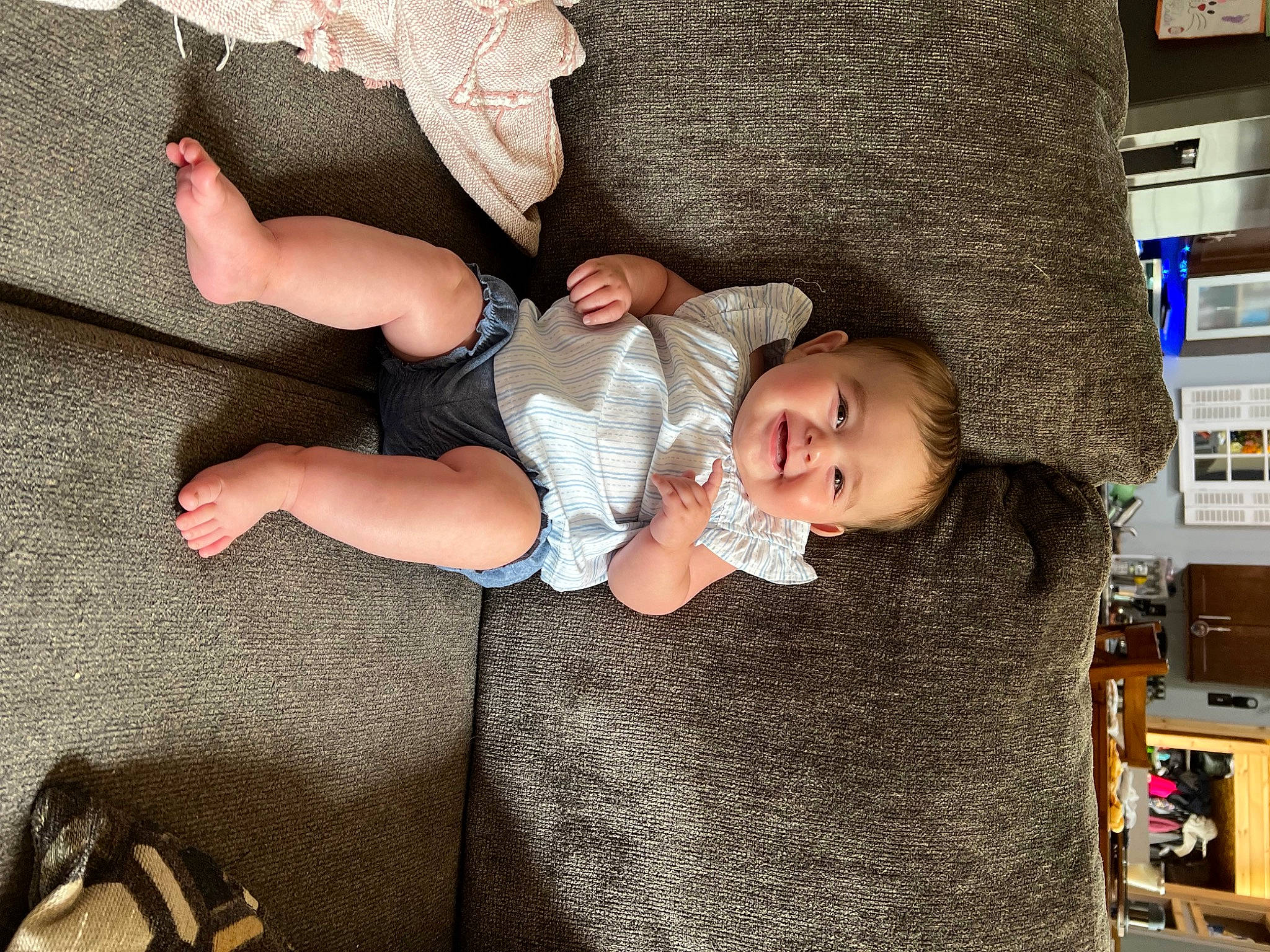 Leighton is registered to the contest to win money with this photo: baby, baby_products, baby_toddler_clothing, child, comfort, couch, flooring, foot, fun, happy, human_leg, joy, lap, person, room, shelf, sitting, smile, sock, thigh