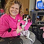 Dixie is registered to the contest to win money with this photo: woman, smiling, puppy, dog, pink_sweater, plush_toy, indoor, living_room, television, furniture, curly_hair, patterned_pants, leopard_print, chair, carpet, cabinet, door, happy, pet, casual