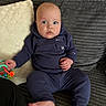 Ezra joined the competition — help win amazing prizes! baby, child, infant, blue_clothing, couch, pillow, toy, hand, foot, face, indoor, person, sitting, curious, wide_eyes, expression, home, soft_texture, hoodie, casual