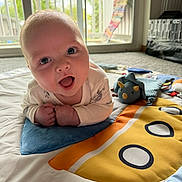 Ezra joined the competition — help win amazing prizes! baby, infant, play_mat, toy, dinosaur_plush, indoor, carpet, window, curious, child, cute, smiling, face, person, colorful, bright, soft, happy, lying, closeup