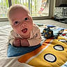 baby, infant, play_mat, toy, dinosaur_plush, indoor, carpet, window, curious, child, cute, smiling, face, person, colorful, bright, soft, happy, lying, closeup