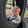 automotive, baby, car, casual, child, clothing, curious, expression, face, gray_sweatshirt, greenery, indoor, parking_lot, person, playful, portrait, tire, toddler, window, young_child
