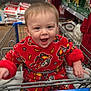 aisle, baby, child, clothing, cute, face, happy, holiday_decorations, indoor, person, playful, red_onesie, retail, shelves, shopping, shopping_cart, smiling, store, toddler, toys