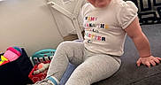 Gianna joined the competition — help win amazing prizes! blinds, casual_clothing, child, couch, earrings, floor, hair, happy, home, indoor, leggings, person, room, shirt, sitting, smiling, sneakers, toddler, toys, window
