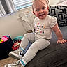 toddler, child, smiling, sitting, indoor, couch, leggings, sneakers, window, blinds, toys, shirt, happy, hair, floor, person, room, earrings, casual_clothing, home