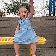 Gianna joined the competition — help win amazing prizes! child, toddler, girl, blue_dress, pink_hearts, yellow_bench, waving_hand, outdoor, sidewalk, brick_wall, trees, cloudy_sky, sandals, happy, smiling, person, casual_clothing, playful, daytime, portrait