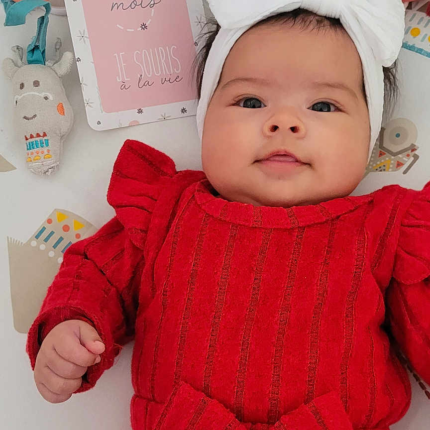 Giovalina a rejoint le concours — aidez-le/la à gagner de superbes lots ! baby, bow, child, cozy, cute, expression, face, hand, headband, indoor, infant, lying_down, milestone_card, playmat, plush_toys, portrait, red_clothing, smiling, soft_toys, young_child