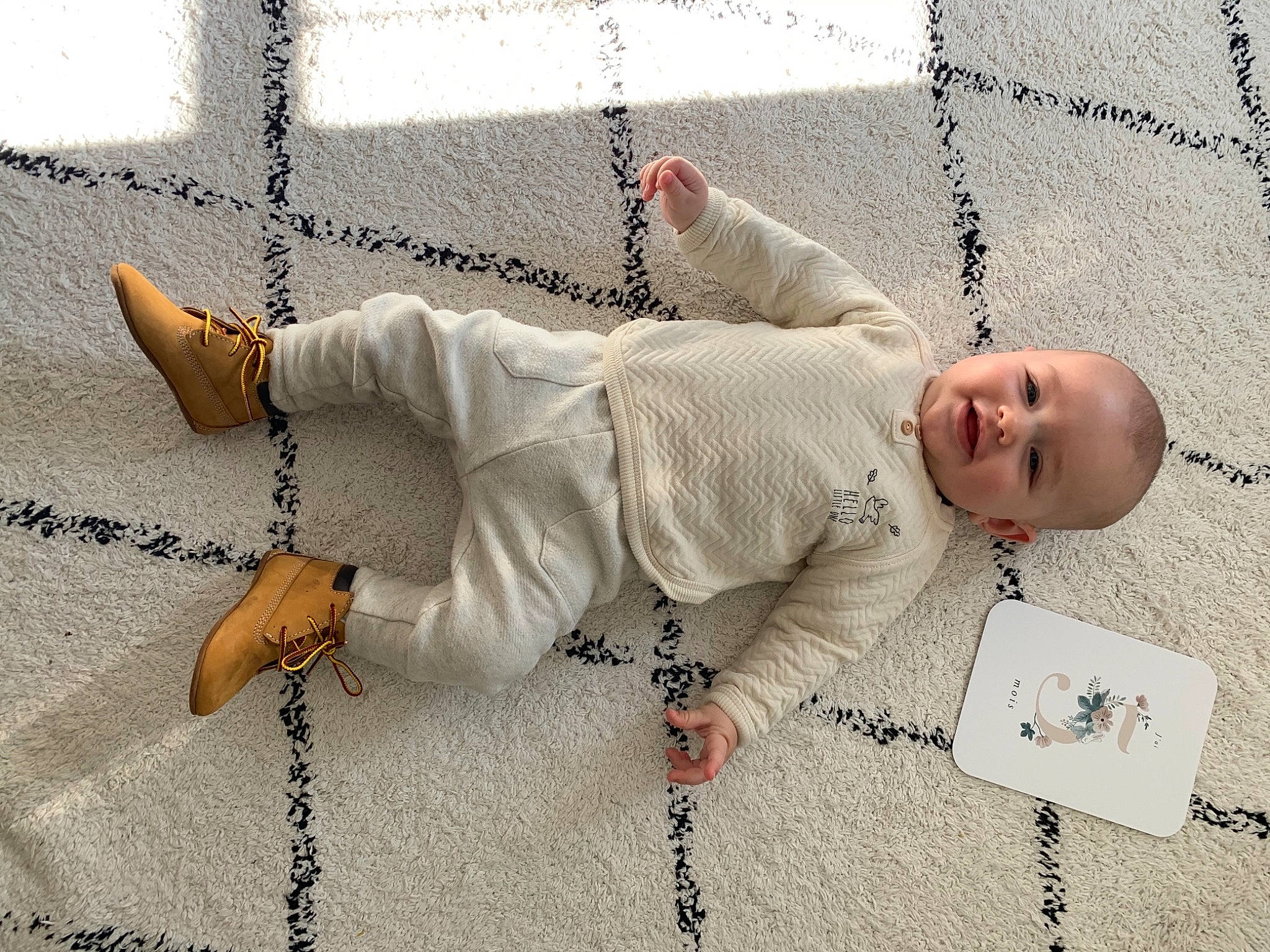 Milo participe au concours pour gagner de l'argent avec cette photo : arm, baby, baby_toddler_clothing, child, comfort, finger, flooring, font, hand, happy, human_body, joint, linens, pattern, person, product, sitting, sleeve, smile, toddler