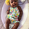 baby, infant, smiling, yellow_headband, colorful_clothing, baby_rocker, cushion, cute, happy, indoors, child, portrait, playful, resting, young_child, expressive_face, headwear, bright_colors, comfortable, adorable