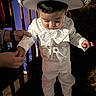 baby, child, toddler, portrait, standing, hat, sparkly_hat, white_suit, formalwear, bow_tie, costume, looking_down, indoor, chair, adult_hands, family, celebration, carpet, decorative_clothing, cute
