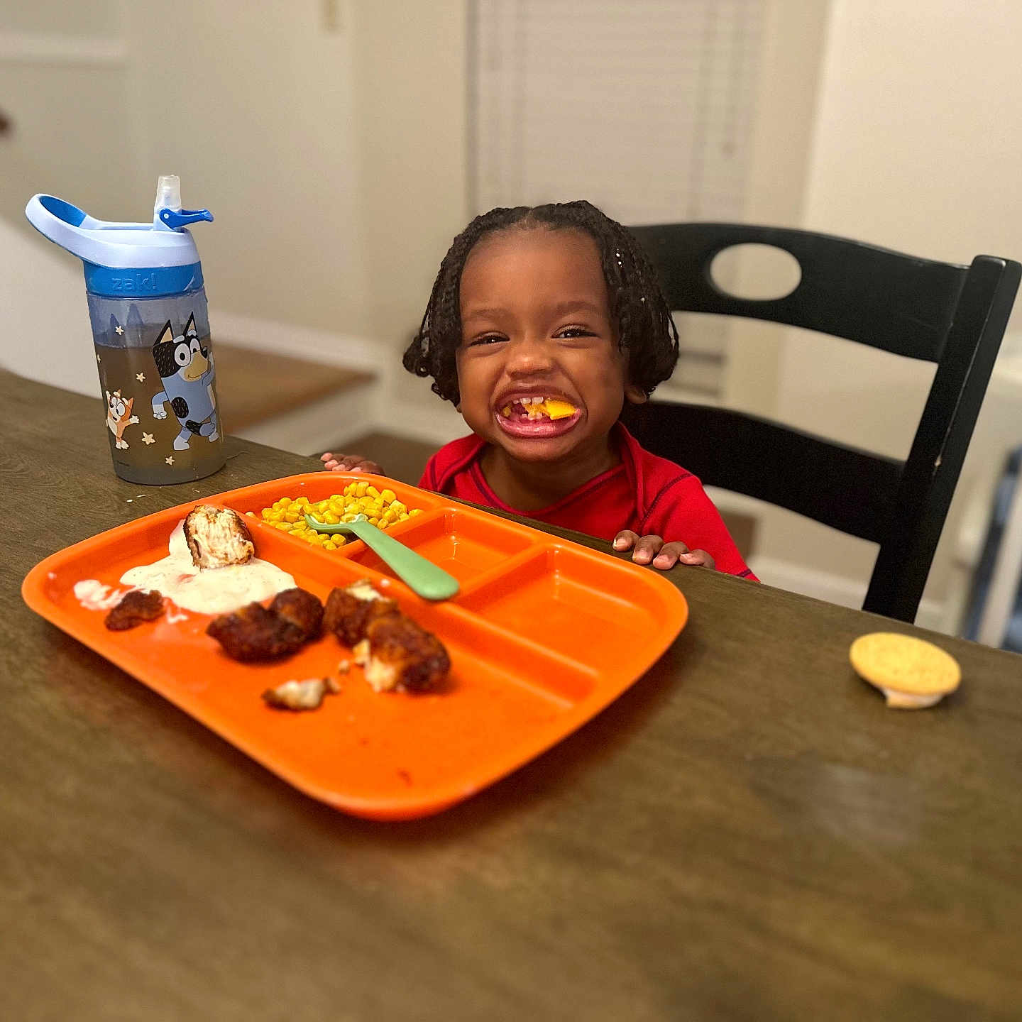 Sy is registered to the contest to win money with this photo: black_chair, braided_hair, chicken_nuggets, child, corn, cute, dining_table, food, fork, happy, high_chair, indoor, meal, orange_plate, person, ranch_dressing, sippy_cup, smiling, toddler, wooden_table