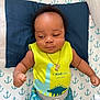 Josiah is registered to the contest to win money with this photo: anchors_pattern, baby, blue_shorts, casual_clothing, child, cute, dinosaur_clothing, eagle_pendant, gold_necklace, indoors, infant, lying_down, patterned_sheet, pillow, portrait, relaxed_expression, sleepwear, small_fists, yellow_shirt, young_child