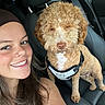 woman, dog, car_interior, leather_seat, harness, curly_fur, smile, nose_ring, long_hair, seatbelt, pet, vehicle, friendship, brown_hair, cute, happy, portrait, travel, companion, indoors