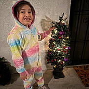 Rosalie Haze joined the competition — help win amazing prizes! celebration, child, christmas_tree, colorful, crocs, decorations, festive, floor, footwear, happy, holiday, indoor, lights, night, onesie, ornaments, person, shadow, smiling, wall