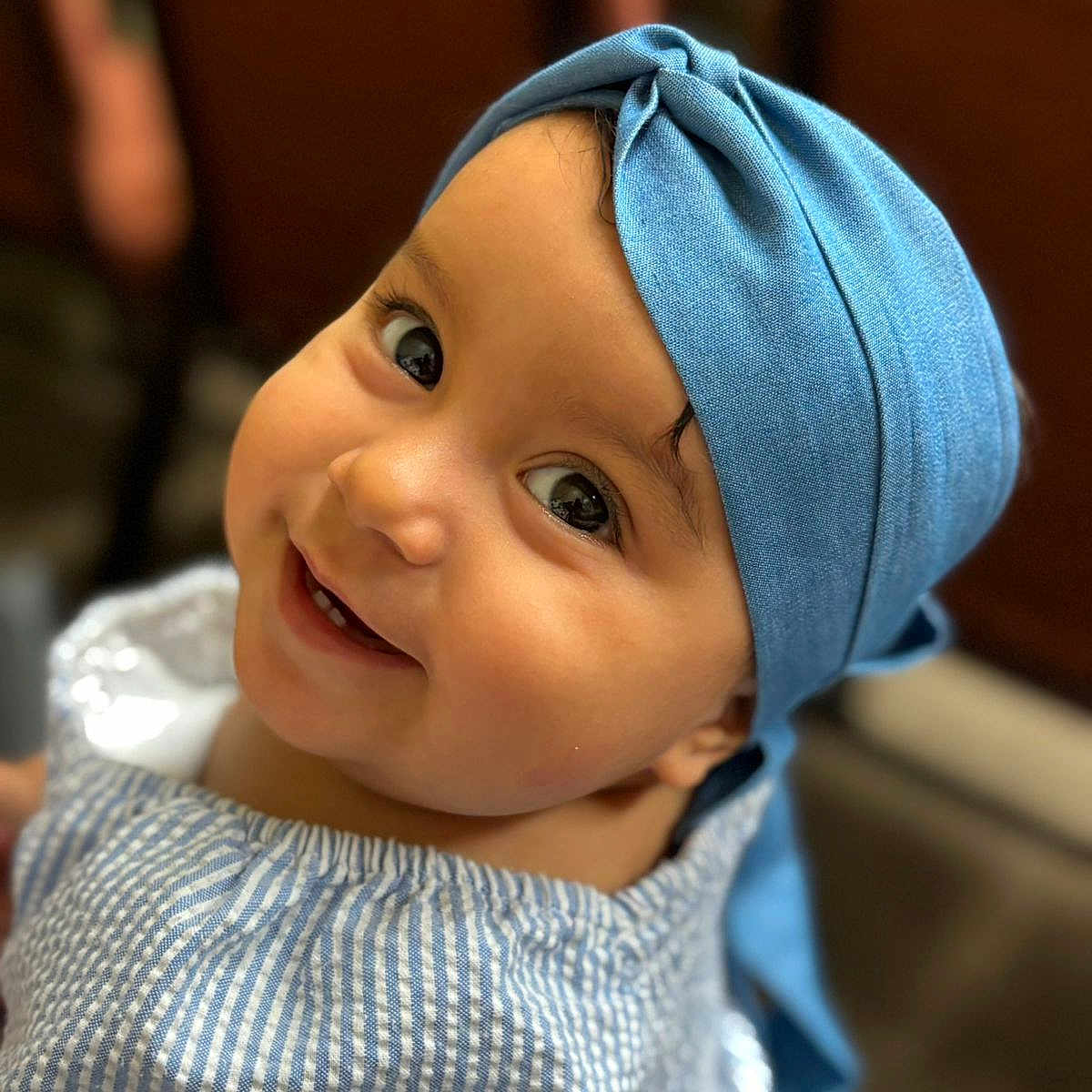 Sol is registered to the contest to win money with this photo: baby, child, smile, blue_headwrap, striped_clothing, portrait, face, cute, happy, indoor, closeup, infant, apparel, headwear, eyes, cheeks, person, furniture, blurred_background, photography