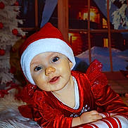 Agathe a rejoint le concours — aidez-le/la à gagner de superbes lots ! baby, child, santa_hat, red_clothing, plush_candy_cane, christmas, holiday, festive, smiling, face, blue_eyes, white_rug, indoor, window, winter_scene, decorations, happy, cute, portrait, holiday_spirit
