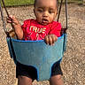 toddler, child, swing, playground, red_shirt, cross_necklace, outdoor, park, wood_chips, grass, stone_wall, daylight, person, baby, hand, legs, metal_chains, seat, casual_clothing, expression