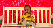 Amir joined the competition — help win amazing prizes! baby, child, bench, smile, yellow_shirt, gray_pants, flower_wall, red_flowers, paper_flowers, white_bench, grass, happy, cute, indoors, portrait, sitting, footwear, colorful, bright, decor