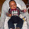 Amir is registered to the contest to win money with this photo: baby, infant, smile, plaid_shirt, bow_tie, suspenders, baby_seat, cushion, toy, pacifier, wooden_floor, clothing, footwear, cute, portrait, indoors, child, happy, person, fashion