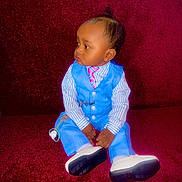 Amir is registered to the contest to win money with this photo: baby, blue_suit, child, clothing, cute, earrings, expression, fashion, footwear, furniture, indoor, pacifier, person, pink_tie, portrait, red_couch, sitting, striped_shirt, toddler, young_child