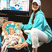 Amarah Love Saunders joined the competition — help win amazing prizes! baby, baby_rocker, blanket, cabinet, cartoon, clothing, crocs, floor, furniture, hat, home, hoodie, indoor, person, smile, socks, television, white_pants, woman, wooden_floor