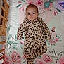 baby, infant, crib, leopard_print, onesie, floral_bedspread, wooden_crib, bedroom, indoors, person, child, cute, sleepwear, patterned_clothing, lying_down, face, eyes, head, pink, green