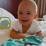 Amarah is registered to the contest to win money with this photo: baby, smiling, toy, bed, white_bed, indoor, child, happy, curtains, pillow, face, infant, clothing, person, cute, lying_down, playtime, room, head, skin