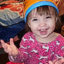 child, toddler, smiling, happy, pink_dress, unicorn_pattern, bucket_hat, orange_bucket, indoor, bedroom, blanket, furniture, wood_floor, toy, person, face, hands, clothing, playful, cute