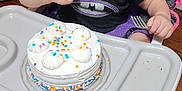 Hayven joined the competition — help win amazing prizes! toddler, child, high_chair, cake, frosting, sprinkles, birthday, indoor, wooden_floor, black_shirt, purple_skirt, pink_ruffle, fork, food, curious, sitting, celebration, young_child, person, cute