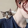 Ashoka is registered to the contest to win money with this photo: cat, tabby_cat, pet, animal, shoulder, person, selfie, portrait, close_up, face, red_hair, blue_shirt, necklace, indoors, furry, whiskers, ears, sleepy, companion, casual