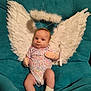 baby, infant, angel, wings, halo, mittens, socks, couch, teal, floral_onesie, costume, cute, portrait, indoors, child, young, seated, soft_texture, decor, adorable