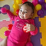 baby, infant, child, onesie, pink_clothing, colorful_balls, foam_mat, playtime, dimples, smile, cute, indoors, playmat, toddler, happy, toy, bright_colors, hand, face, lying_down