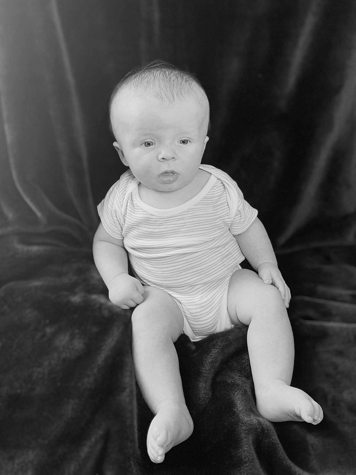 Theo is registered to the contest to win money with this photo: arm, baby, black, black_and_white, cheek, child, eye, face, facial_expression, head, monochrome, monochrome_photography, people, person, photograph, photography, sitting, skin, standing, toddler