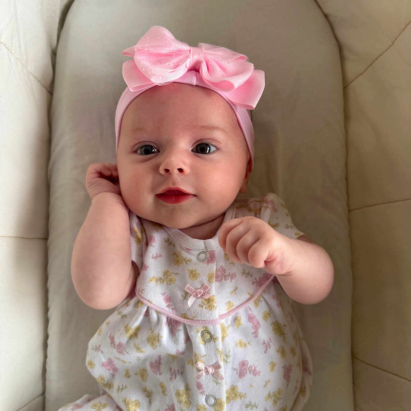 Eleia is registered to the contest to win money with this photo: adorable, baby, child, comfort, cushion, cute, expression, face, floral_pattern, hand, headband, indoors, infant, lying_down, onesie, pink_bow, portrait, skin, small_person, soft_fabric