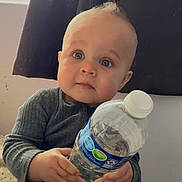 Leo joined the competition — help win amazing prizes! baby, child, water_bottle, indoor, curtain, window, sitting, clothing, blue_eyes, hands, face, person, cute, infant, portrait, soft_light, curious, bottle, casual, young