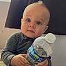 baby, child, water_bottle, indoor, curtain, window, sitting, clothing, blue_eyes, hands, face, person, cute, infant, portrait, soft_light, curious, bottle, casual, young