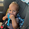 baby, blue_toy, buckled, car_interior, car_seat, child, curious, eyes, face, hands, infant, patterned_fabric, portrait, safety_harness, short_hair, smiling, striped_shirt, sunlight, toy, vehicle