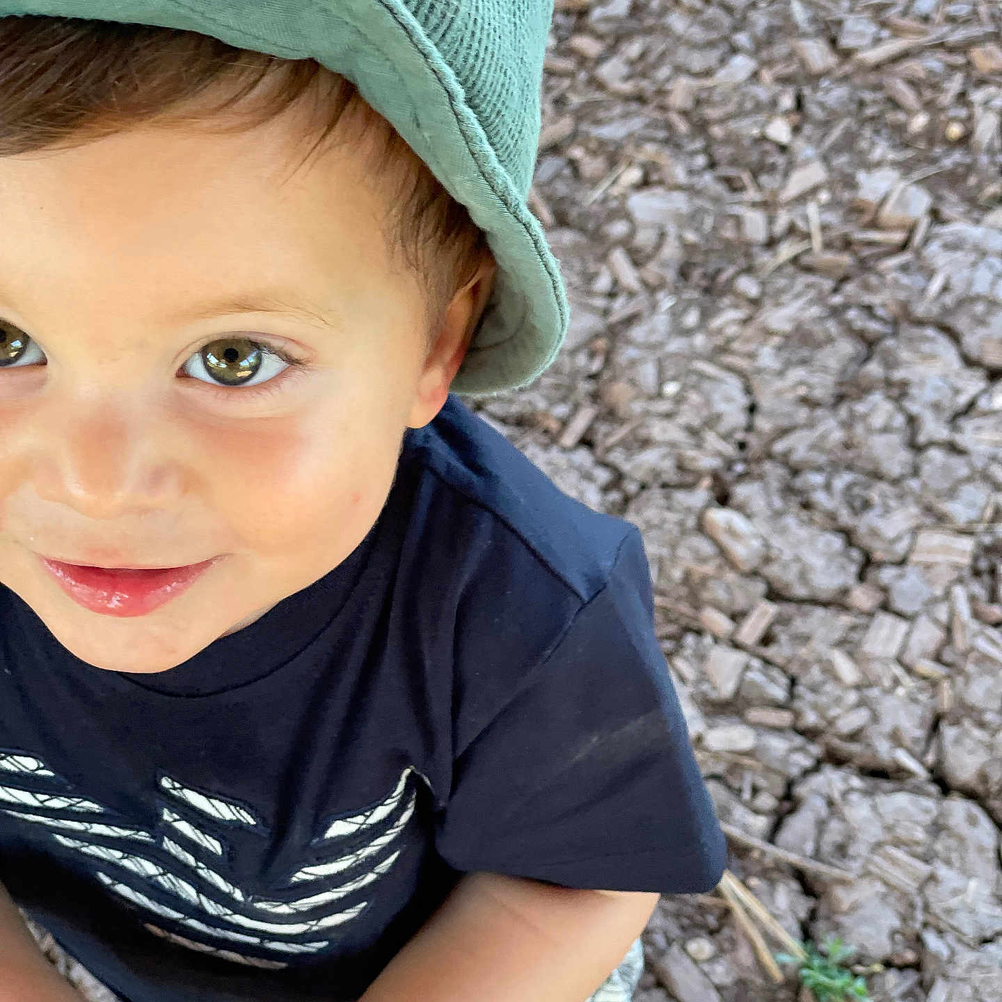 Nolan participe au concours pour gagner de l'argent avec cette photo : bucket_hat, casual_clothing, child, cute, daylight, dirt, expression, eyes, ground, hand, hat, nature, outdoor, person, play, rock, shirt, smile, toddler, young_child