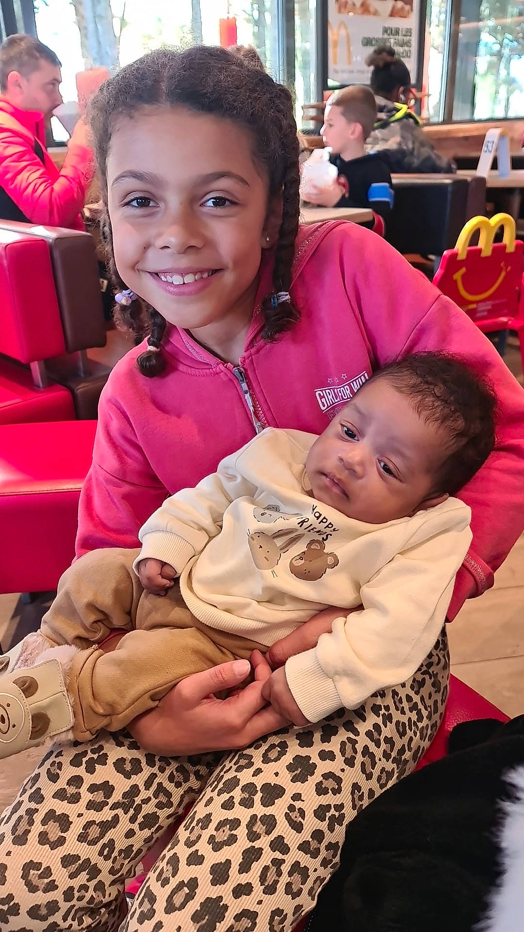 Kehwan a rejoint le concours — aidez-le/la à gagner de superbes lots ! baby, braids, casual, chair, child, clothing, family, fast_food, food_court, girl, happy, holding, indoor, infant, leopard_print, people, restaurant, seated, smile, table