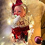 Nelya a rejoint le concours — aidez-le/la à gagner de superbes lots ! baby, infant, christmas, holiday, dress, red_bow, headband, pacifier, blanket, fairy_lights, ornament, smiling, cute, soft_lighting, indoors, festive, toddler, cozy, warm, celebration