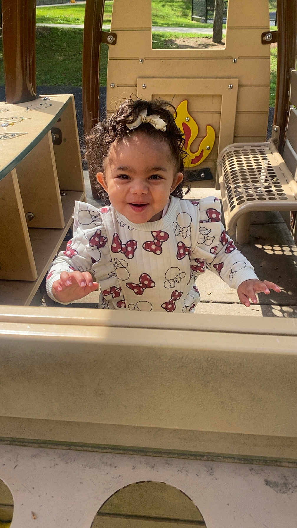 Luna joined the competition — help win amazing prizes! toddler, child, playground, curly_hair, bow, sweater, patterned_clothing, outdoor, sunlight, happy, smiling, play_structure, metal_bench, grass, daylight, person, cute, young_child, expression, park