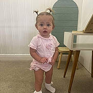 Nellie joined the competition — help win amazing prizes! toddler, child, indoors, pink_clothing, socks, bow, pony_tail, carpet, wooden_chair, table, curious, standing, young_child, cute, frills, baby, person, room, wall_paneling, floor