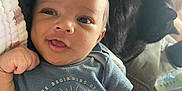 Jensen is registered to the contest to win money with this photo: baby, infant, child, blue_shirt, text_on_clothing, cat, black_cat, pet, couch, indoor, person, cute, smiling, happy, face, hand, relaxing, cozy, home, animal