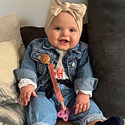 Tess participe au concours pour gagner de l'argent avec cette photo : baby, child, smiling, denim_jacket, headband, bow, pacifier_clip, couch, pillow, blue_eyes, socks, casual_clothing, indoor, happy, seated, infant, cute, portrait, cozy, hands