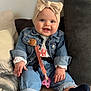baby, child, smiling, denim_jacket, headband, bow, pacifier_clip, couch, pillow, blue_eyes, socks, casual_clothing, indoor, happy, seated, infant, cute, portrait, cozy, hands